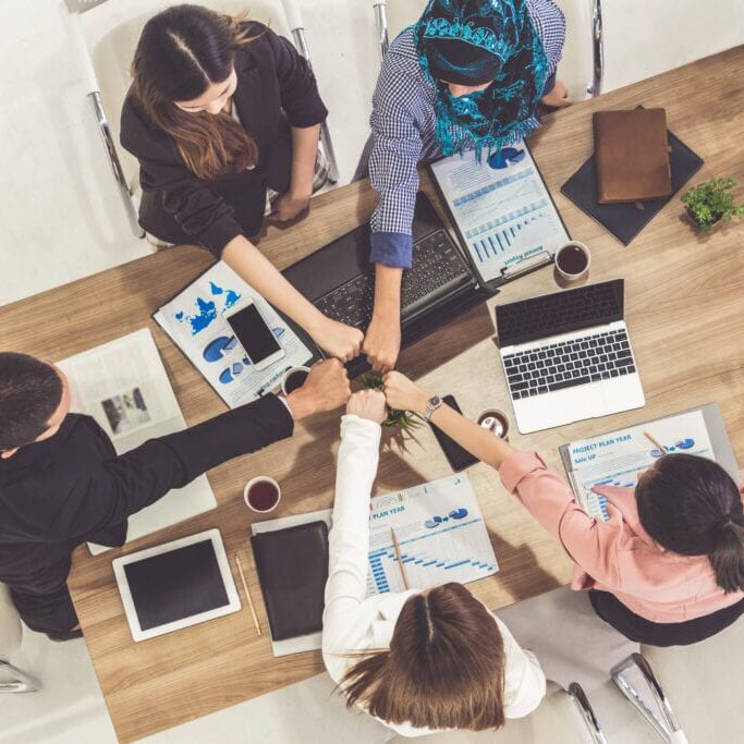Businessmen and businesswomen joining hands in group meeting at multicultural office room showing teamwork, support and unity in business. Diversity workplace and corporate people working concept.